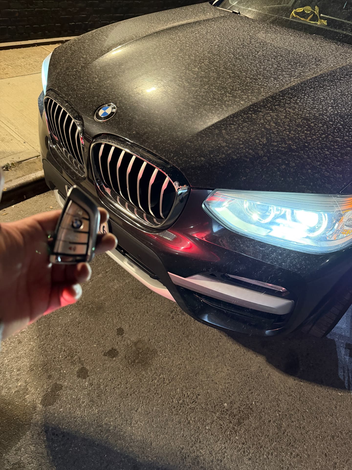 New BMW smart key held in front of a BMW X-series at night